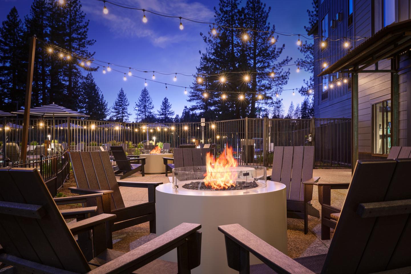 Cozy patio with fire pit, Adirondack chairs, string lights, and evening sky.