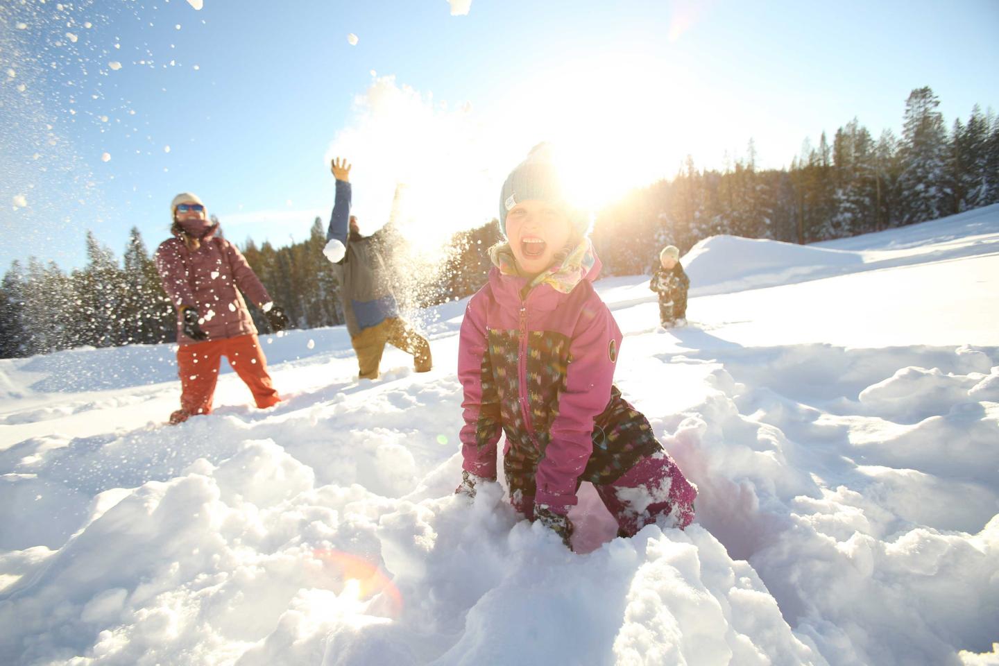 Children playing joyfully in the snow under a bright sunlit sky.
