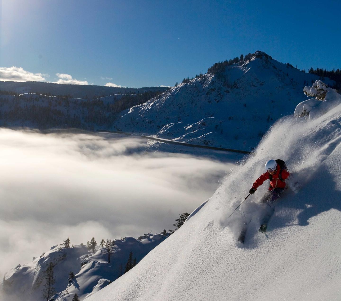 Skier in red descends snowy mountain under clear blue sky.